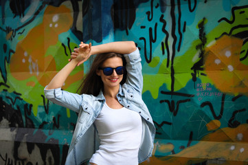 young woman posing in a white t-shirt, blue denim shirt and blue glasses on graffiti background
