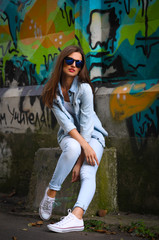 young stylish girl sitting near a concrete wall which is all covered in graffiti