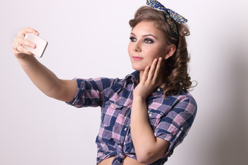 Pinup pretty girl in checkered shirt makes selfie by smartphone in studio