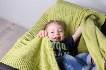 Cute little boy plays in green plaid on couch in room, top view