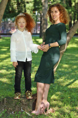 Obraz premium Happy little girl with her mother stand near trees in summer green park