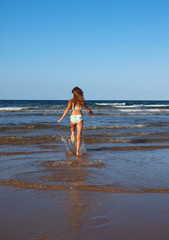 Braungebranntes sportliches Mädchen im Bikini rennt am Strand in die Wellen vor strahlend blauem Himmel