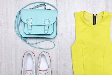 Light green blouse, white sneakers and handbag. Fashionable concept. Wooden background.