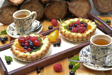 Colored and fresh raspberry, redcurrant, blackcurrant, kiwi on pie, tart and cup of tea on log background