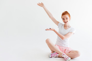 Happy ginger woman girl sitting on floor and showing something