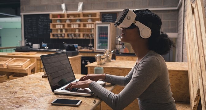 Woman using virtual reality headset while working on laptop