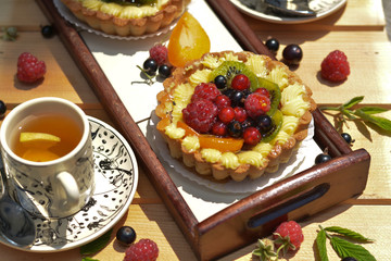 Summer sweet tart with raspberry, redcurrant, blackcurrant, kiwi and a cup of tea on wooden texture