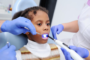 a dark-skinned baby girl in the dentist's chair.dentist treats your child's teeth with a dark complexion. The UV lamp in the patient's mouth