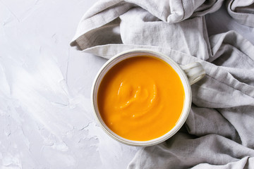 Bowl of vegetarian pumpkin carrot soup served on textile napkin over gray concrete background. Top view with copy space