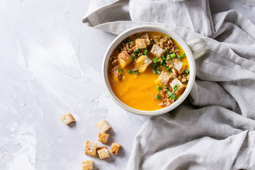 Bowl of vegetarian pumpkin carrot soup served with croutons and onion on textile napkin over gray...