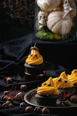 Halloween decorated sweet dessert table black cupcake with orange cream, white meringue ghosts with chocolate eyes on metal tray, leaves acorn decor skulls and pumpkin over black tablecloth.