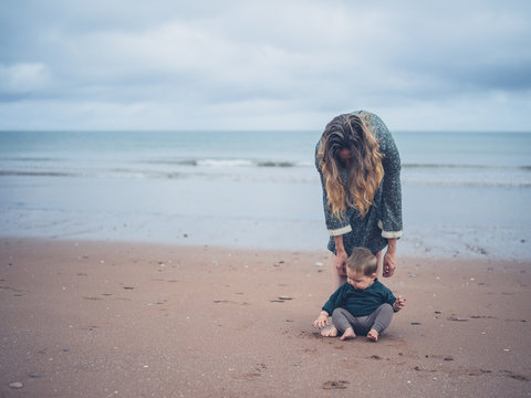 Mother helping baby walk on beach