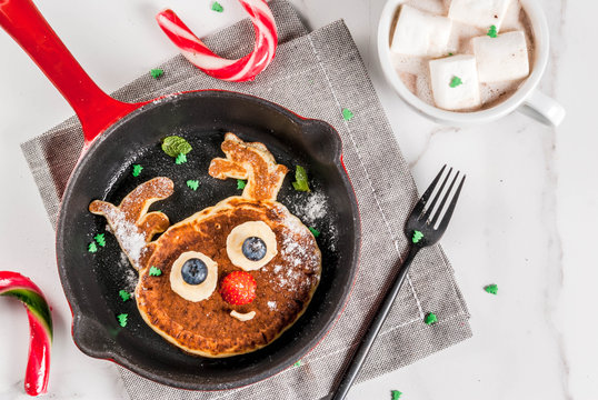 Funny food for Christmas. Kids breakfast pancake decorated like reindeer, with hot chocolate with marshmallow, white table copy space top view