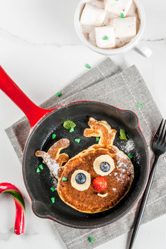 Funny food for Christmas. Kids breakfast pancake decorated like reindeer, with hot chocolate with marshmallow, white table copy space top view