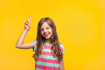 Cheerful little girl pointing up on orange