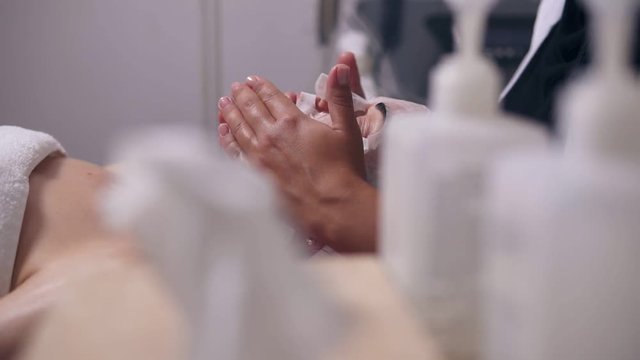Professional cosmetologist holding her hands on woman's face while apllying special mask on client's face and neck. Camera movement through bottles with special treatment. Professional carboxytherapy