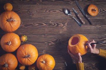 Preparations to Halloween. Hands drawing jack-o-latern on pumpkin over wooden background, top view,...