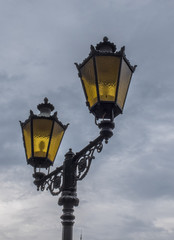 Fototapeta na wymiar Detail of antique wrought iron street lamp and yellow glass over cloudy sky