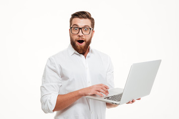 Shocked young bearded man using laptop. - obrazy, fototapety, plakaty