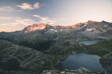 High altitude alpine lake, dams and water basins in idyllic land with majestic rocky mountain peaks glowing at sunset. Wide angle view on the Alps.