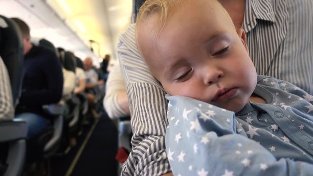 Baby is sleeping in plane with mom in her arms