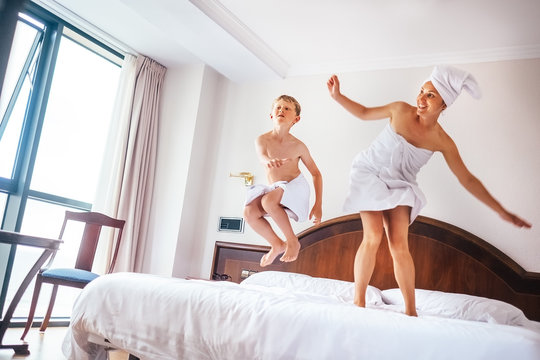 Mother and son jump on bed in luxury hotel room
