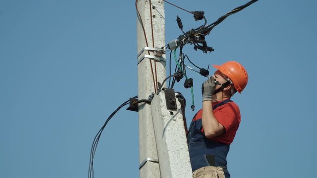 An electrician working at a newly installed utility pole - connects a new power line.