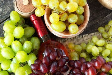 Bunches of fresh different ripe  grapes and a bottle of red wine on a blue wooden textural surface. space for advertising text 