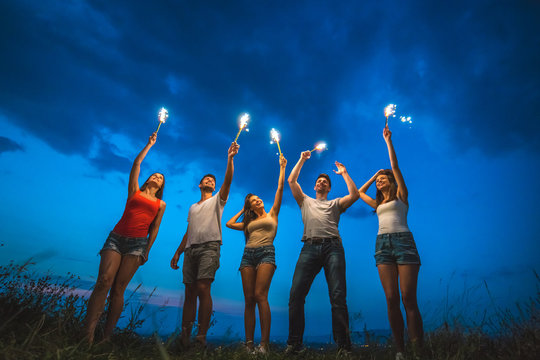The happy five people hold firework sticks. evening night time