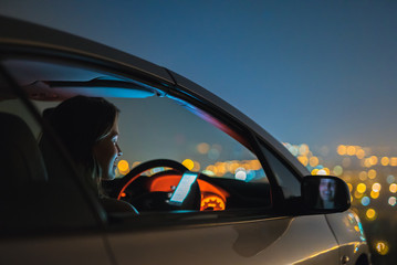 The attractive woman phone in the car on the background of the city. night time
