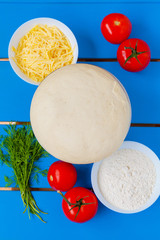 Pizza dough with ingredients on blue wooden table.