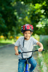 Obraz premium Little boy learns to ride a bike in the Park near the home. Portrait of a cute kid on bicycle. Happy smiling child in helmet riding a cycling.