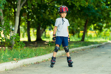 Little boy riding on rollers in the summer in the Park. Happy child in helmet learning to skate.
