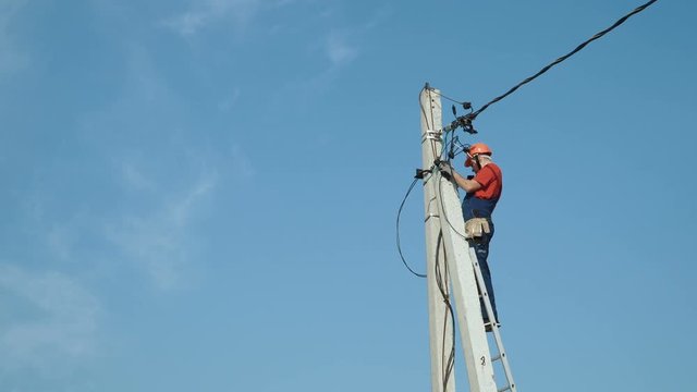 An electrician working at a newly installed utility pole - connects a new power line.