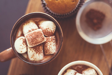 Cups with hot chocolate with marshmallow and muffins on dark wooden desk. Selective focus. Toned Image