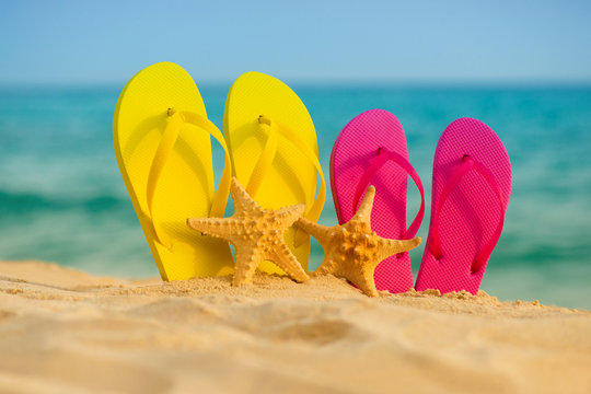 Sea-stars with yellow and pink sandals stand in the sand against the background of the sea.