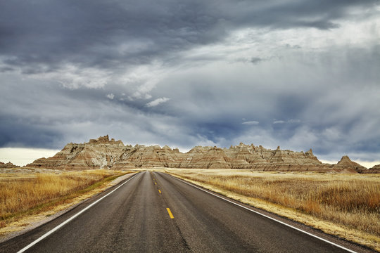 Picturesque road in Badlands National Park with stormy sky, travel concept background, South Dakota, USA. 