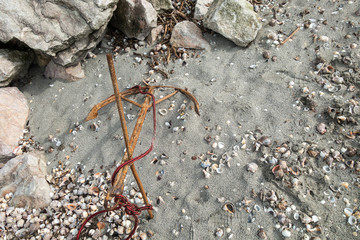 Old rusty anchor abandoned on sand, near rocks 