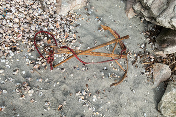 Old rusty anchor abandoned on sand, near rocks 