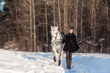 Fototapeta na wymiar Nice girl and white horse in a forest in a winter