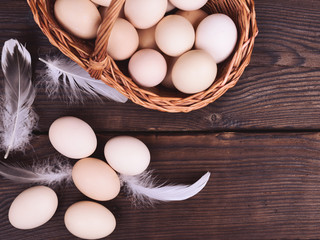 chicken eggs in a wicker basket on a wooden brown table, top view