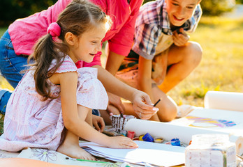 Happy mother and two kids are painting in the park. The concept of a happy family.