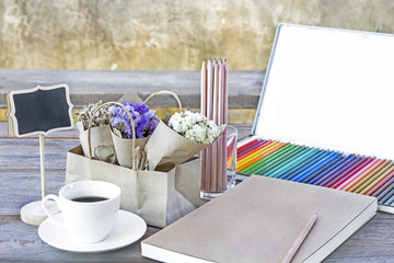 Colorful Color pencils for art drawing.Notebook of blank pages with coffee cup and flower bouquet on wooden table background.