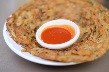 Dish of crispy Thai fried omelet with herb and pork (Thai traditional cooking style), served with Sriracha hot chili sauce on saucer.