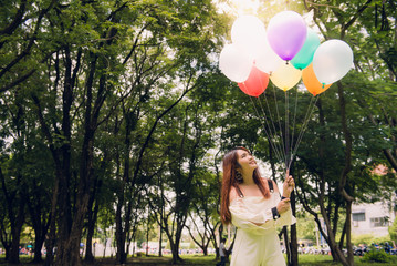 Smiling young beautiful asian women with long brown hair in the park. With rainbow-colored air balloons in her hands.sunny and positive energy of nature.