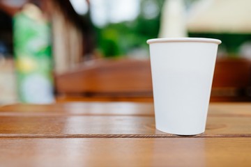 White paper coffee cup on wooden table outdoors.