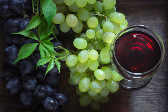 Glass of red wine with ripe grape on a wooden background. Close up and top view.