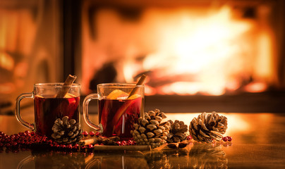 Mulled wine glasses on table in front of burning fireplace.