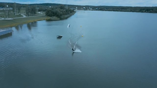 OVERHEAD aerial drone shot of female wake boarding in a cable wakepark on a lake. 4K UHD 60 FPS 