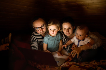 Young parents with little children and laptop at night.